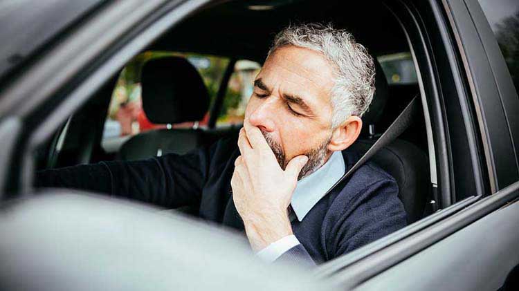 Man yawning at the wheel of a car trying not to fall asleep