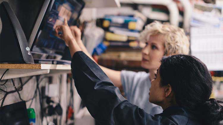 Two woman pointing at a monitor to better understand questions for the mechanic