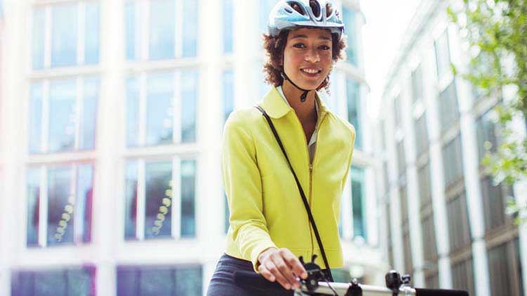 Una mujer yendo a trabajar en bicicleta y con un casco en la cabeza